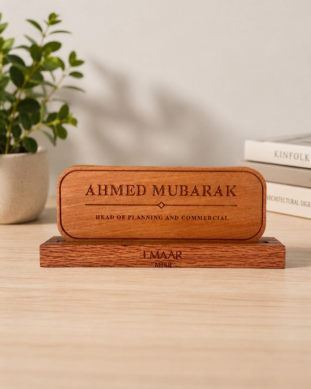 A personalized wooden plaque engraved with Name and his title, resting on a matching wooden base on a light wood tabletop. Corporate gift, desk plate