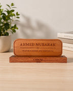 A personalized wooden plaque engraved with Name and his title, resting on a matching wooden base on a light wood tabletop. Corporate gift, desk plate