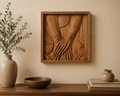 A square framed wooden wall art piece with a carved relief design of hands, displayed on a beige wall above a wooden console table with a vase, bowl, and books.